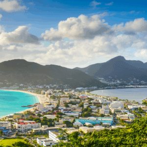 Coastal town with a turquoise bay sandy beach and green hills under a cloudy blue sky at noon