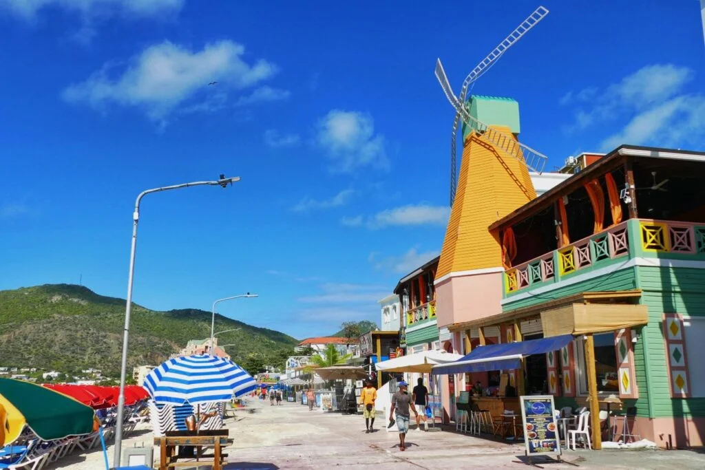 Colorful beachfront street with a tall yellow building topped by a wind sculpture outdoor seating and umbrellas