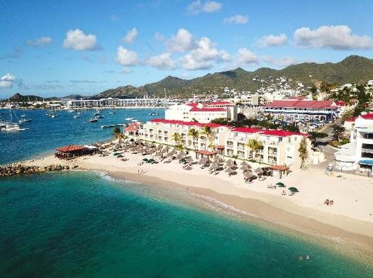 A seaside resort with a sandy beach turquoise water and white buildings with red roofs along the shore