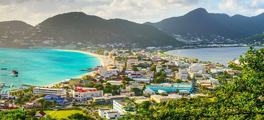 Coastal town along a turquoise bay with a sandy beach colorful buildings boats and green hills in the distance