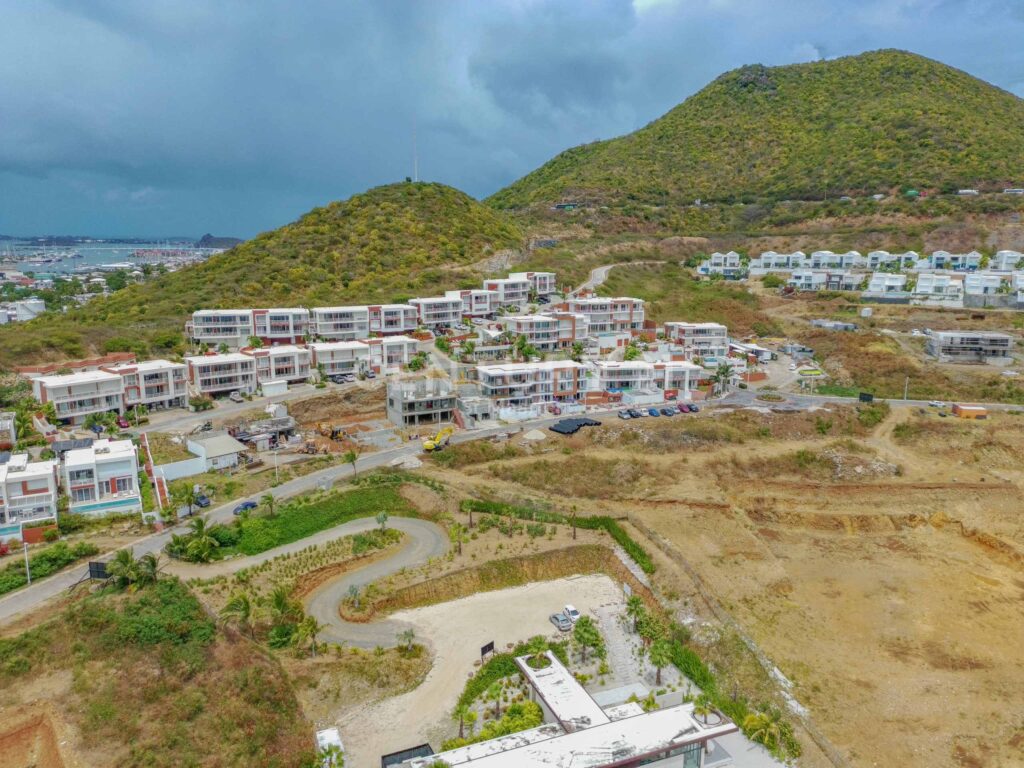 PTSC_0182-scaled-2 - Wei Landgraf Aerial view of a coastal hillside neighborhood under construction, with white modern townhouses along curved roads and sparse vegetation.