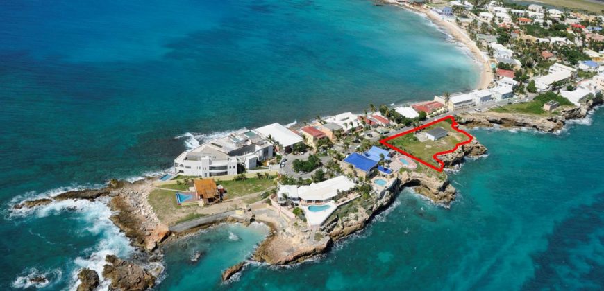 WhatsApp-Image-2024-02-19-at-075731_bce22f5e-870x420-1 - Wei Landgraf Aerial view of a coastal neighborhood with a red-outlined property on the rocky shore next to turquoise water and white houses.