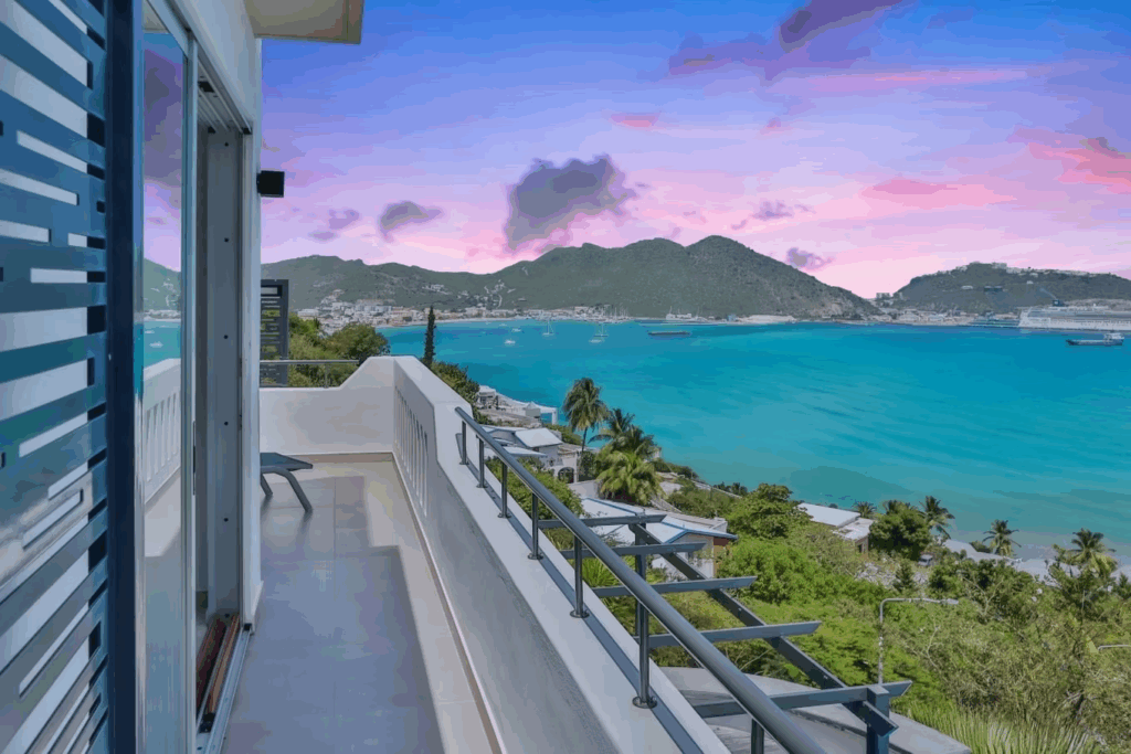 f7228d_7b107148142545be97f0a51a5108dbbfmv2-Edited-1024x683-1 - Wei Landgraf Balcony view over turquoise sea with boats, palm trees, and distant mountains at sunset/sunrise.