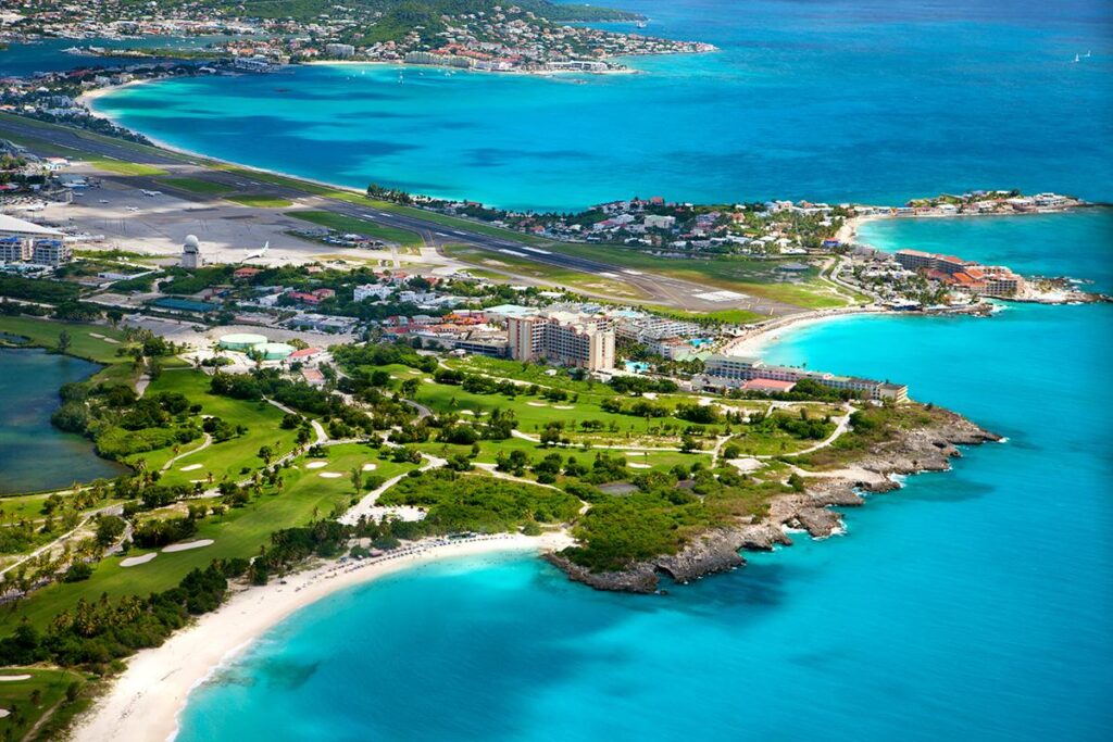 st-maarten-properties-condos-apartments-mullet-bay-towers-02 - Wei Landgraf Aerial view of a tropical island with turquoise beaches, a golf course, and a small coastal town.