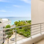 Balcony with a metal railing overlooking a tropical resort and the blue sea.